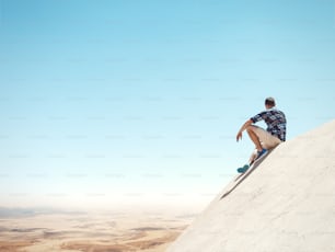 Young man sitting on a top of the cliff and looking at the desert