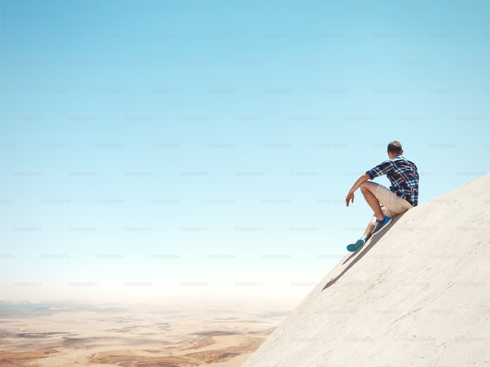 Young man sitting on a top of the cliff and looking at the desert