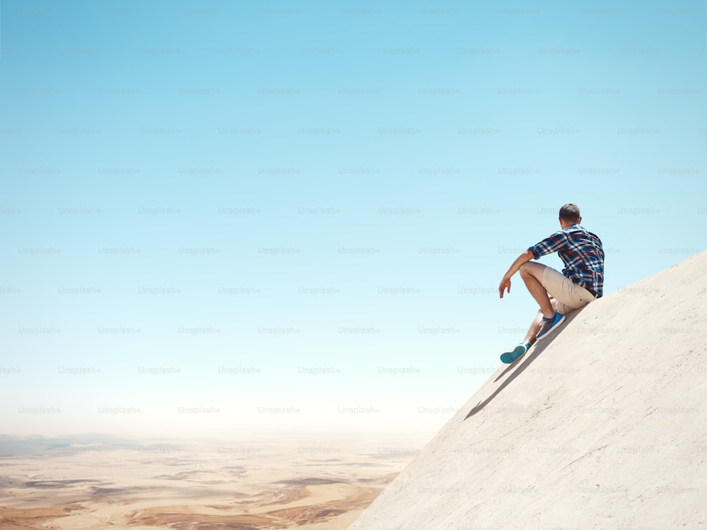 Junger Mann sitzt auf einer Spitze der Klippe und schaut auf die Wüste
