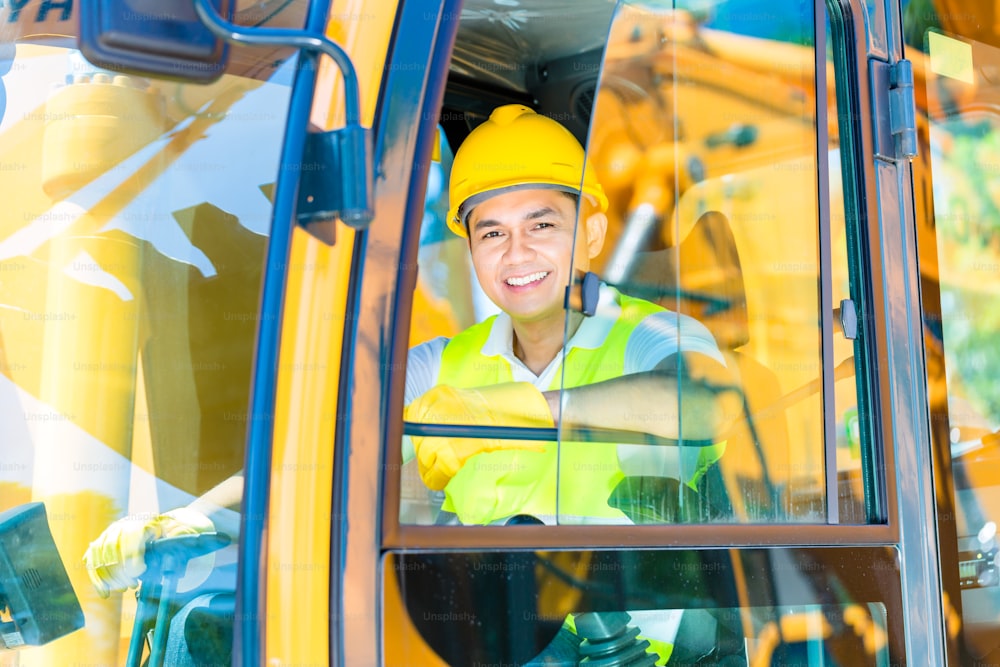 Asian driver sitting in cockpit of construction machinery of building site or mining or rental company