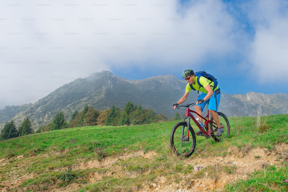 Um jovem macho que monta uma bicicleta de montanha ao ar livre no prado