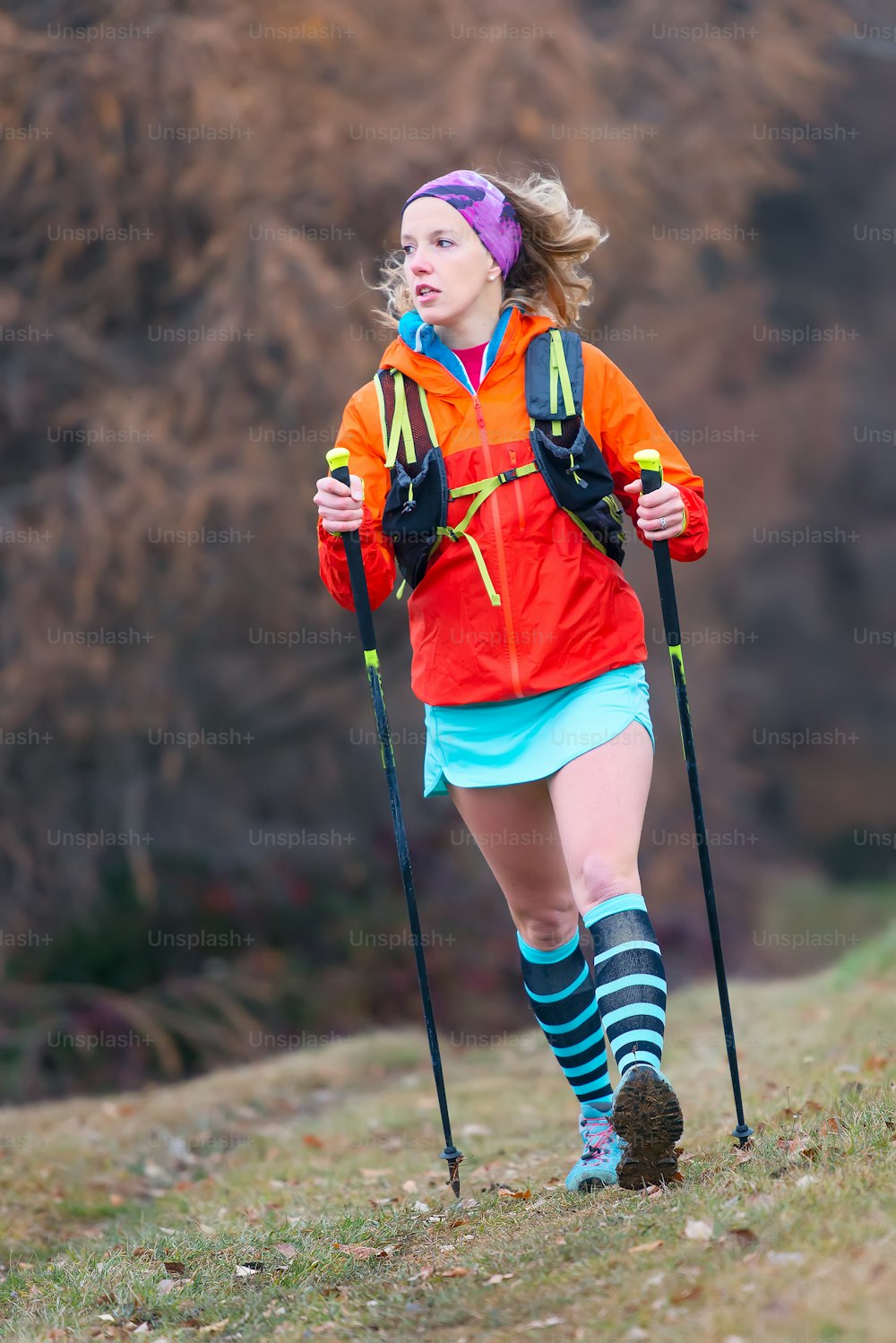 Joven deportista rubia practica activamente la marcha nórdica en un prado de montaña