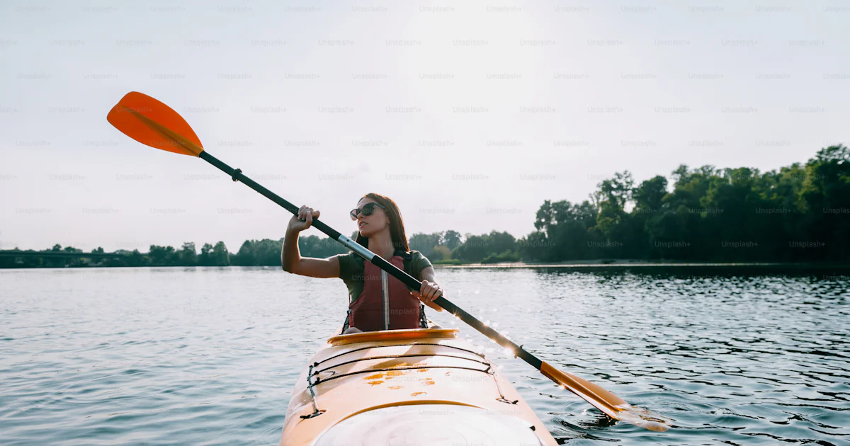 Front view of beautiful young smiling woman kayaking on lake and ...