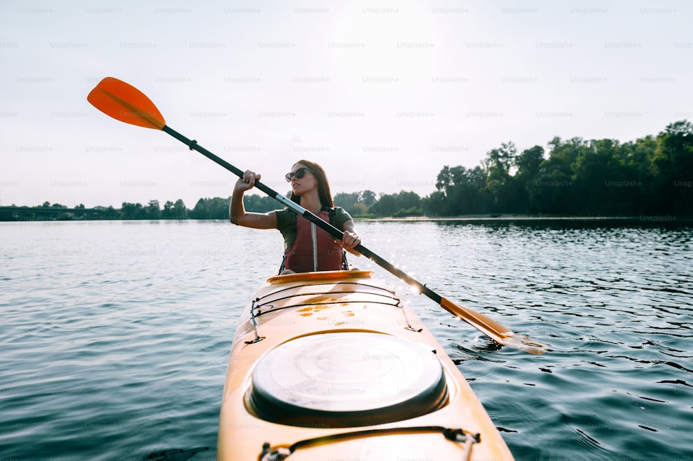 Front view of beautiful young smiling woman kayaking on lake and smiling