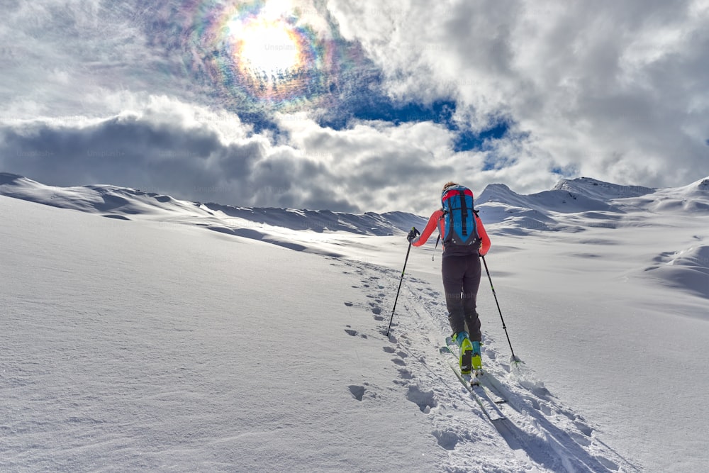 Chica cuesta arriba con pieles de foca y esquí de montaña en los Alpes