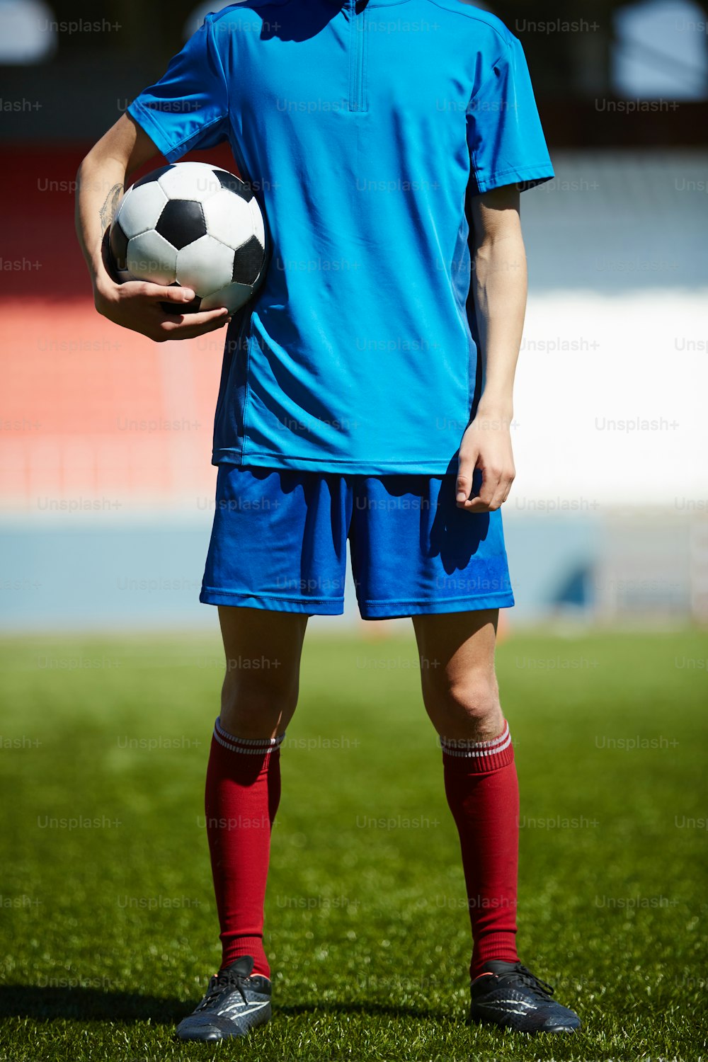 Young footballer with soccer ball standing on the field