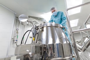 caucasian scientist in blue lab suit and gloves stand on platform and look in the chromed barrel, look at camera, turned