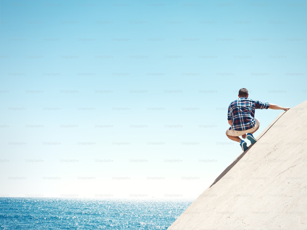 Young man sitting on a peak and looking at the sea