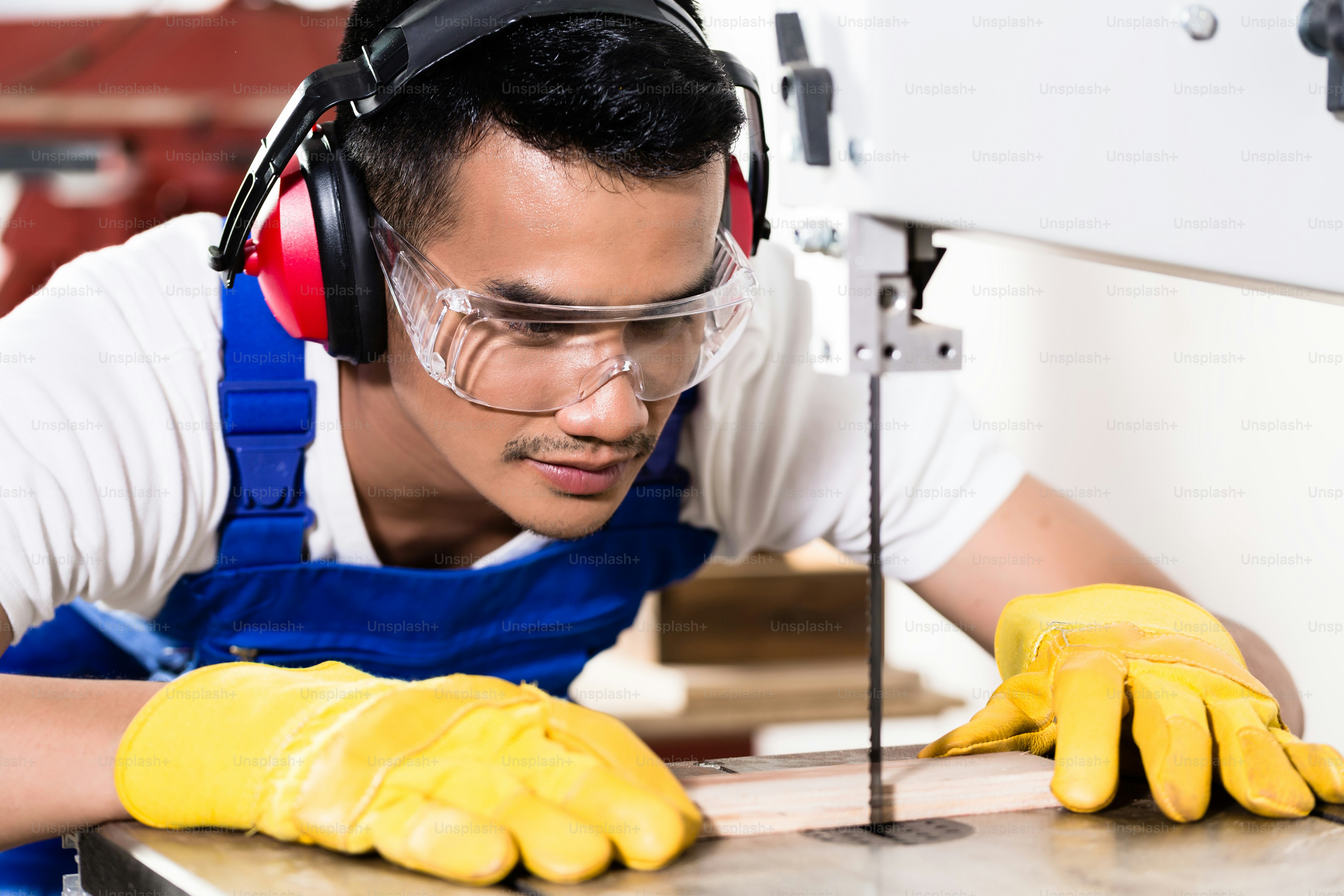 Asian carpenter or worker on saw cutting wood in workshop