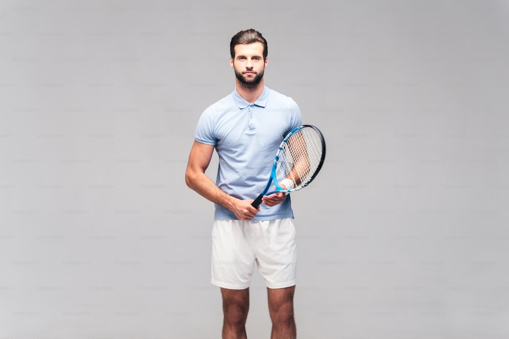 Handsome young man in sports clothing carrying tennis racket and looking at camera