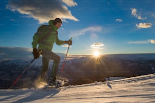 Mann übt Schneeschuhwandern in einem suggestiven Sonnenuntergang in den Bergen