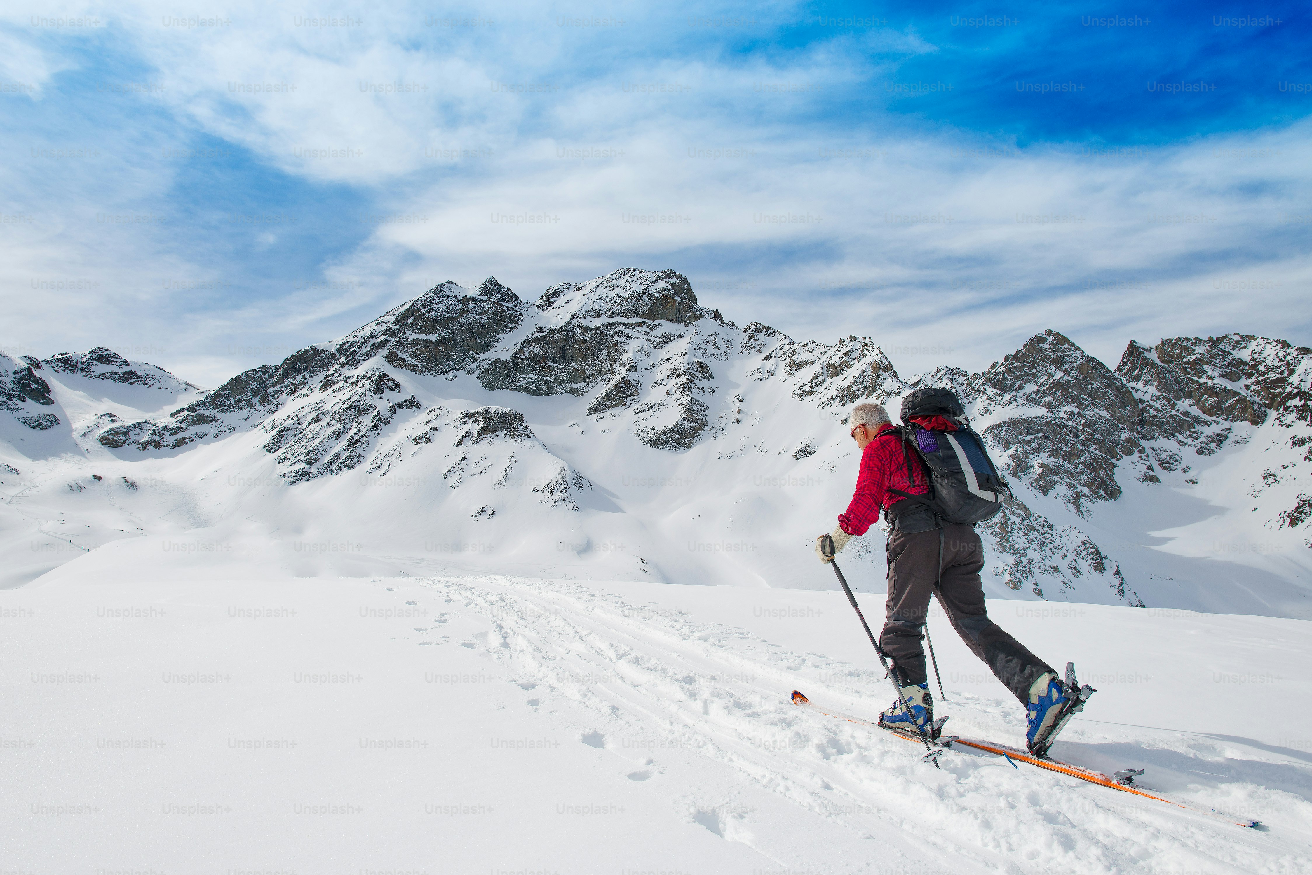 Elderly man sporting fit skis uphill climbing in te alps