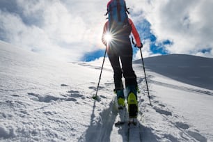 Muchacha montañera sube en esquís y pieles de foca hacia el sol