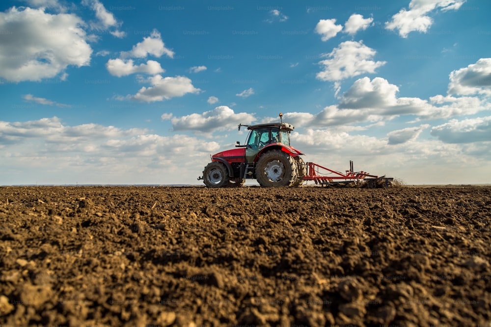 Agricultor en tractor preparando la tierra con cultivador de semillero