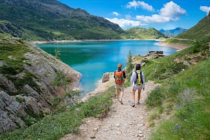 Dos amigos durante una caminata en las montañas caminando por un sendero cerca de un lago alpino