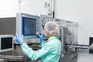 trabalhador de fábrica caucasiano em traje de laboratório azul verificar leituras da máquina, olhar para o painel de controle