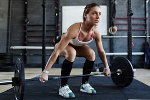 Entrenamiento extremo: atleta femenina musculosa que comienza el ejercicio con barra de pie en posición de sentadilla