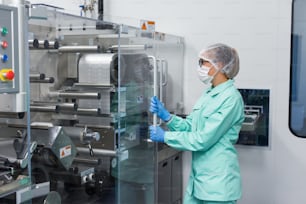 trabalhador de fábrica caucasiano no trabalho de terno de laboratório azul com máquina, máquina com painéis de vidro