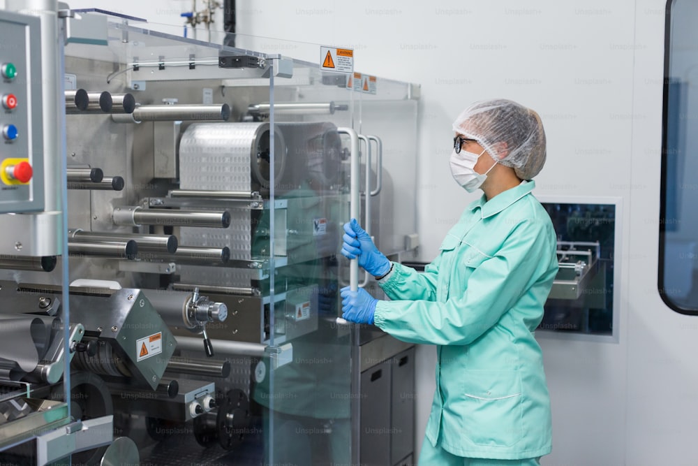 Trabajador caucásico de fábrica en traje de laboratorio azul trabajo con máquina, máquina con paneles de vidrio