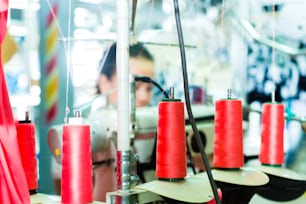 Spools of an industrial sewing machine in a factory, in the background woking a seamstress