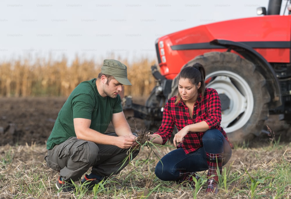 Jovens agricultores examinando a sujeira enquanto o trator está arando o campo