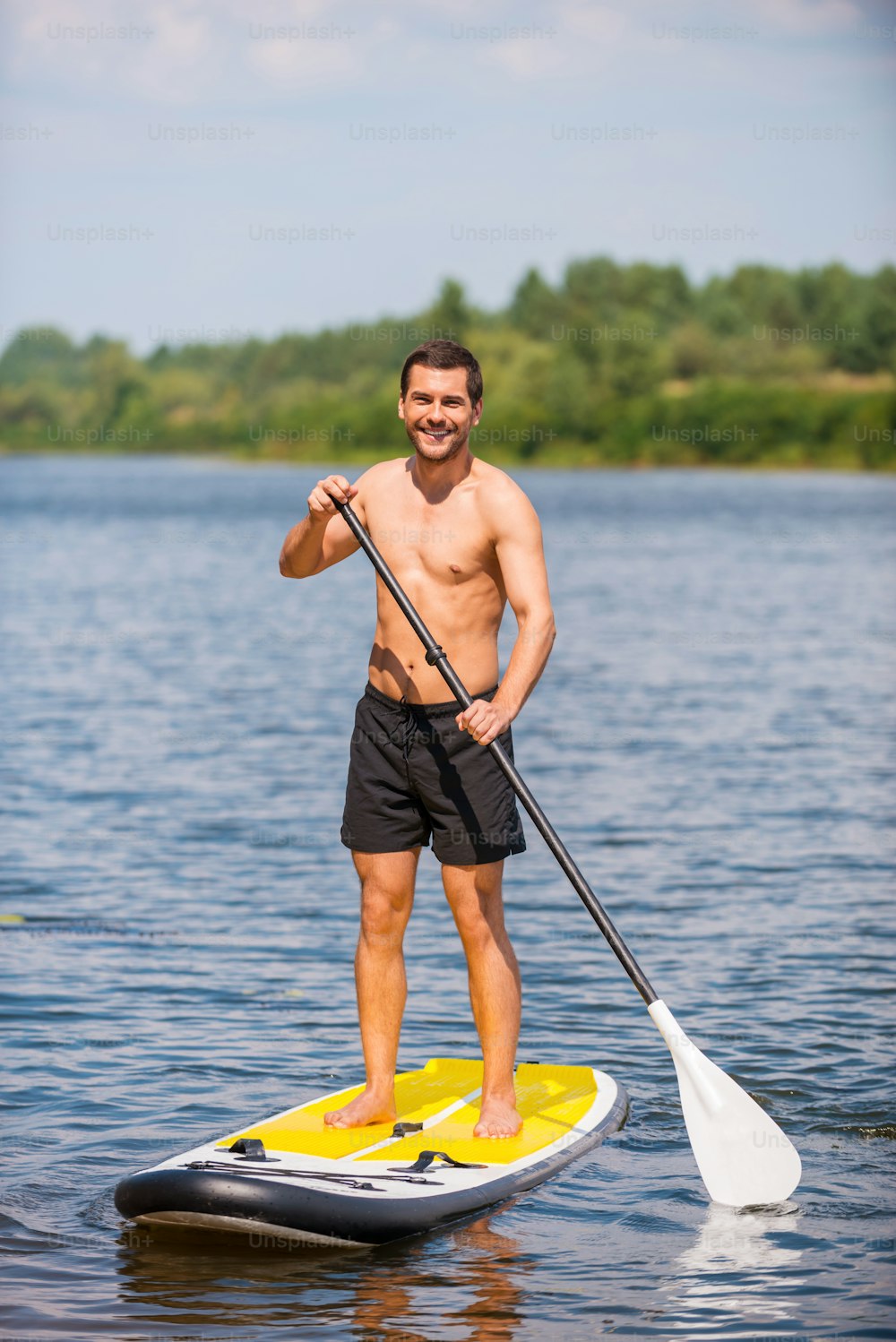 Handsome young man surfing on his paddleboard and smiling