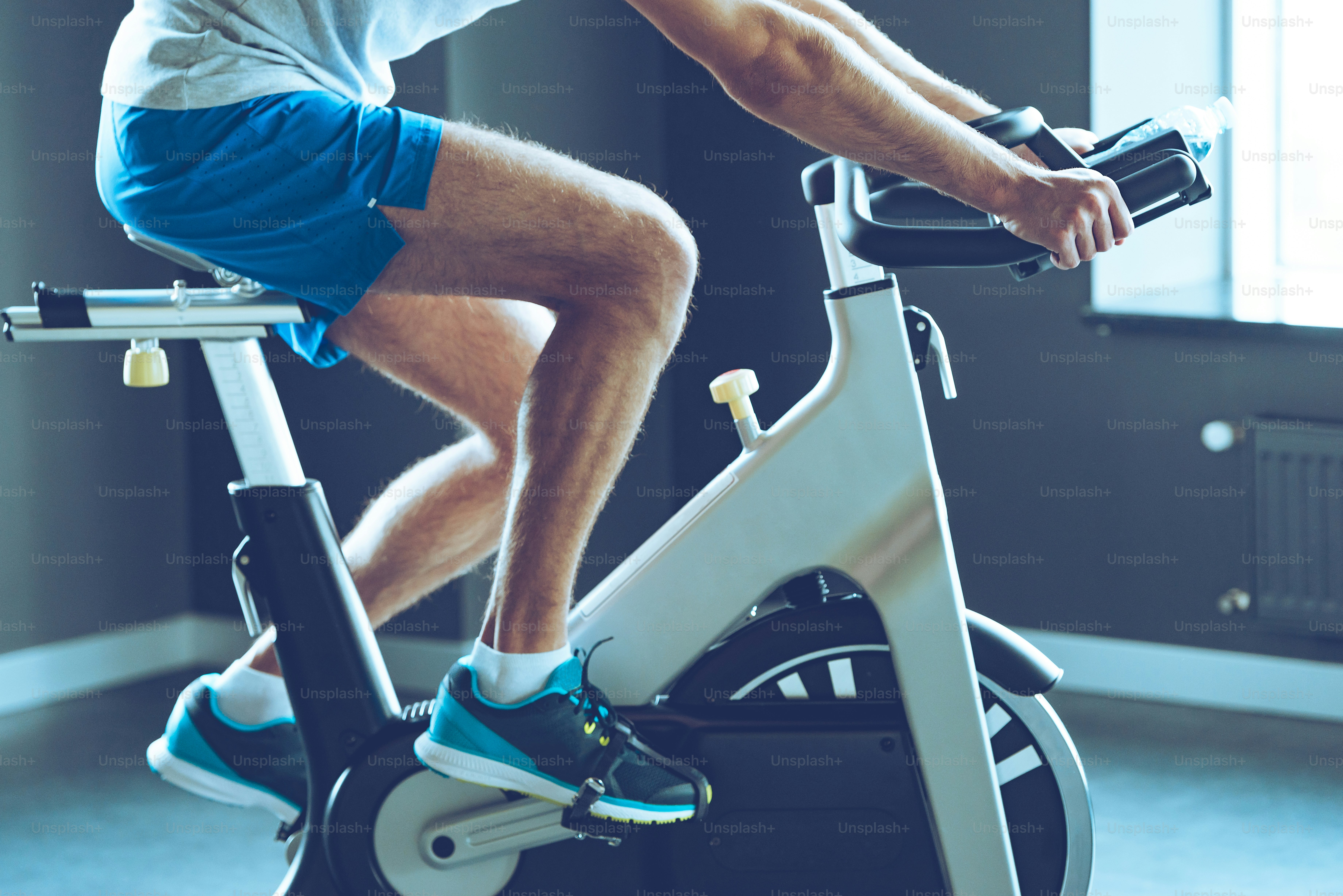 Side view part of young man in sportswear cycling at gym