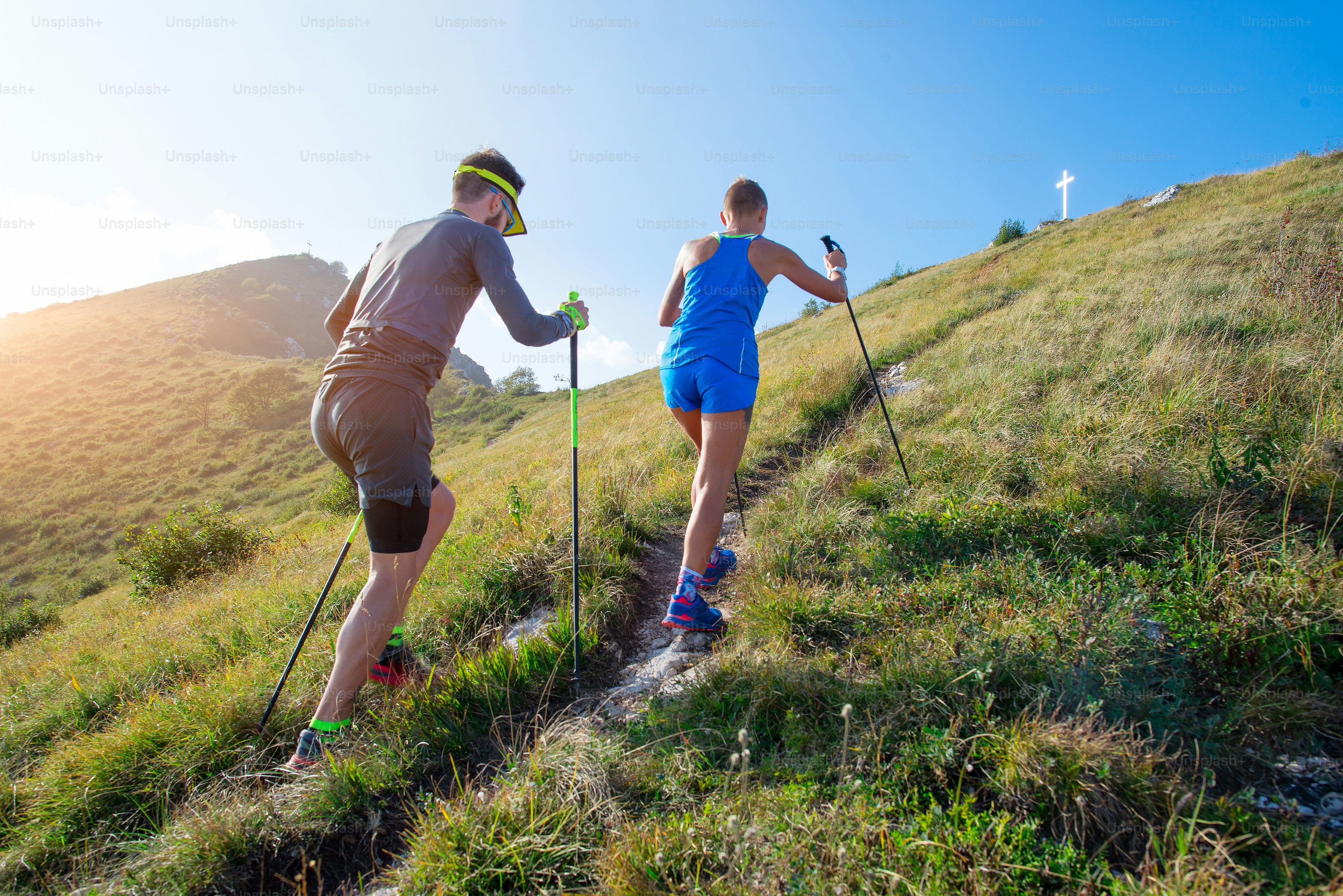 Trail running in the mountains a couple with sticks prepares to the top ...