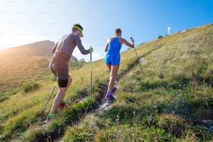 Trail running en la montaña, una pareja con palos se prepara para llegar a la cima