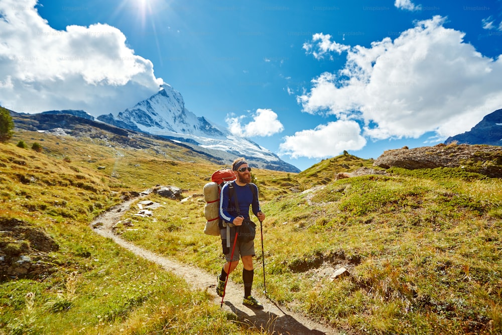 リュックサックを背負ってアプルス山地のトレイルを歩くハイカー。マッターホルン山付近のトレッキング