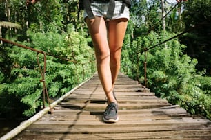 Woman's legs with backpack walking across hanging bridge in tropical forest