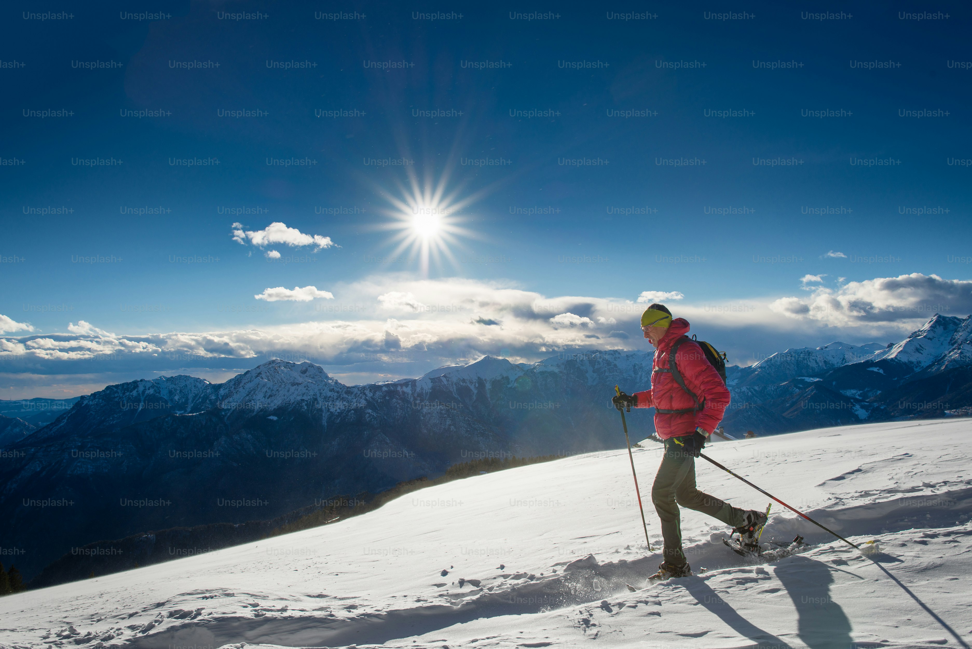 Der Mann in Schneeschuhen und mit Trekkingstöcken Im Hochgebirge in der Sonne