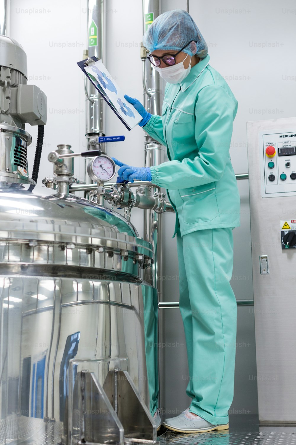 foto verticale, scienziato in uniforme blu da laboratorio controlla come funziona il serbatoio del compressore, tablet in mano