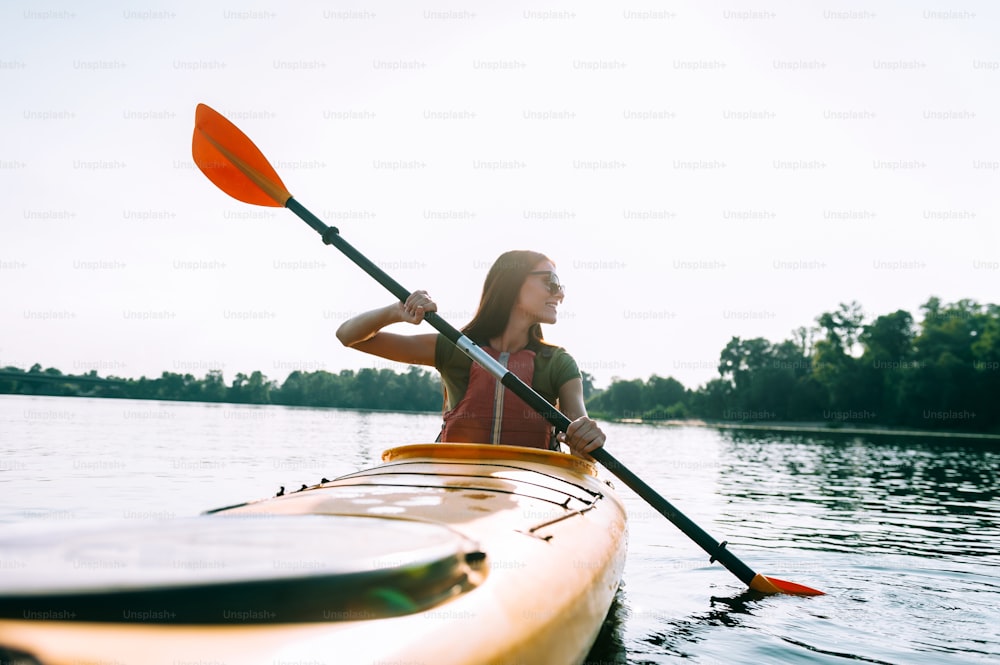 Bella giovane donna sorridente che va in kayak sul lago e guarda oltre la spalla con sorriso