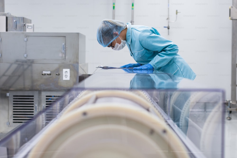 Operaio caucasico in abito da laboratorio blu, con tablet in mano, piegarsi sulla macchina di produzione