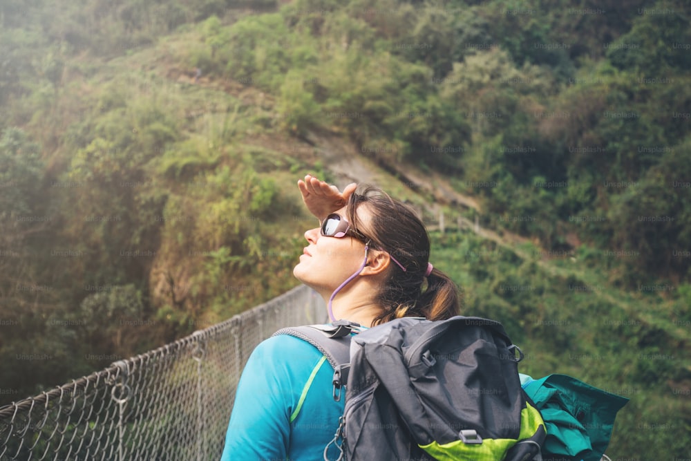 Traveling girl with backpack on suspension bridge.