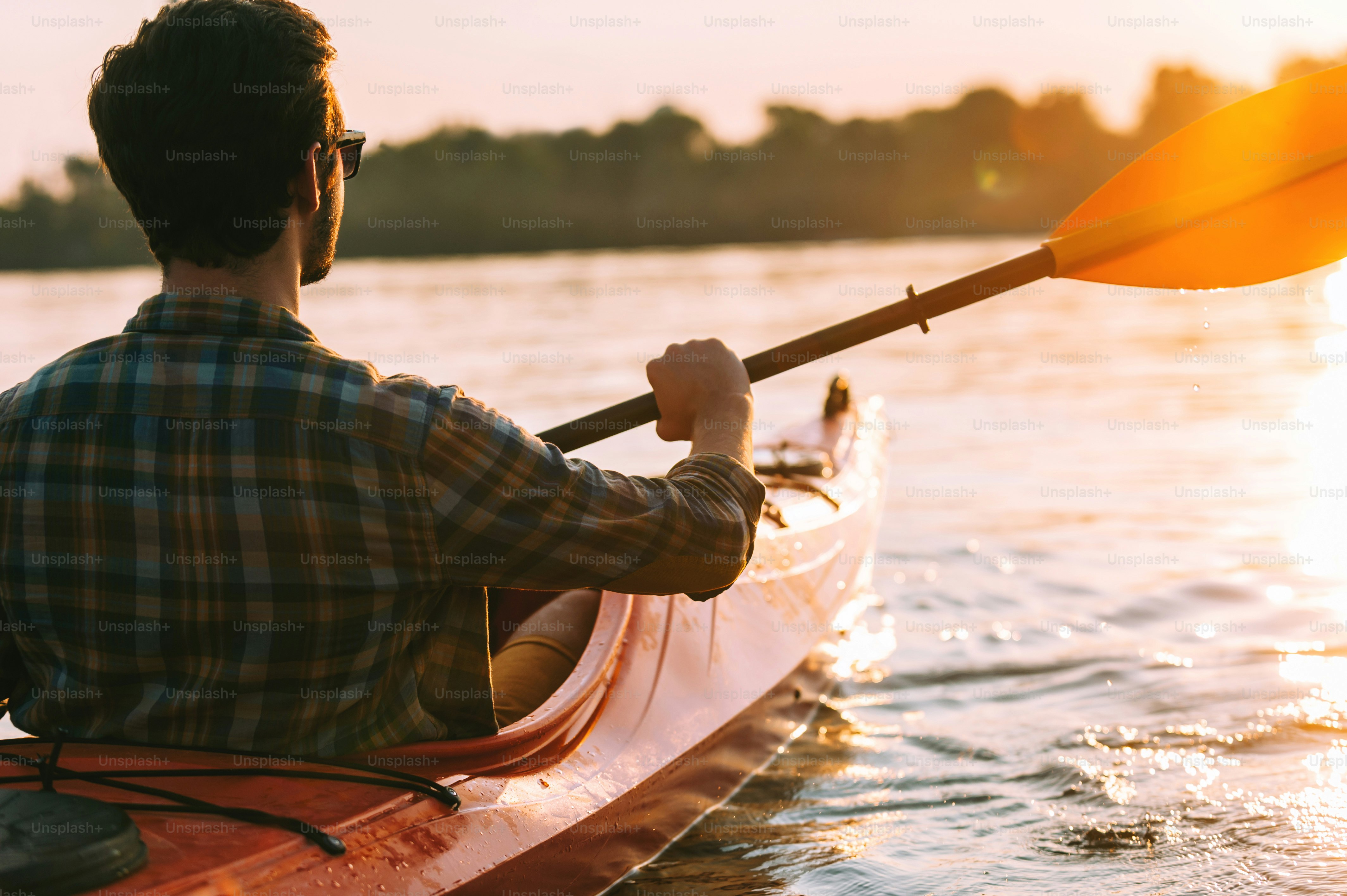 Rear view of young man kayaking on lake with sunset in the background