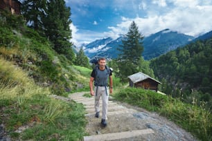 erwachsener Wanderer im Aplser Gebirge. Wanderung in der Nähe des Matterhorns. Ein Mann mit glücklichem Gesicht auf dem Weg auf den Almwiesen mit Landhäusern