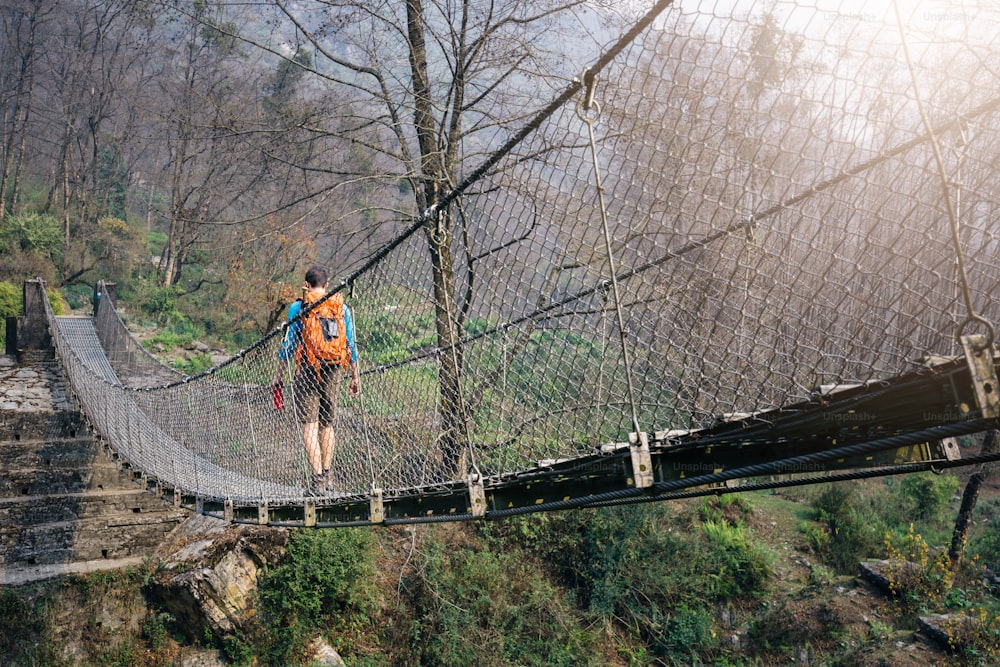 Turista con zaino che attraversa la passerella sospesa sull'Himalaya.