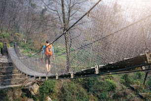 Tourist with backpack crossing suspension footbridge at Himalayas.