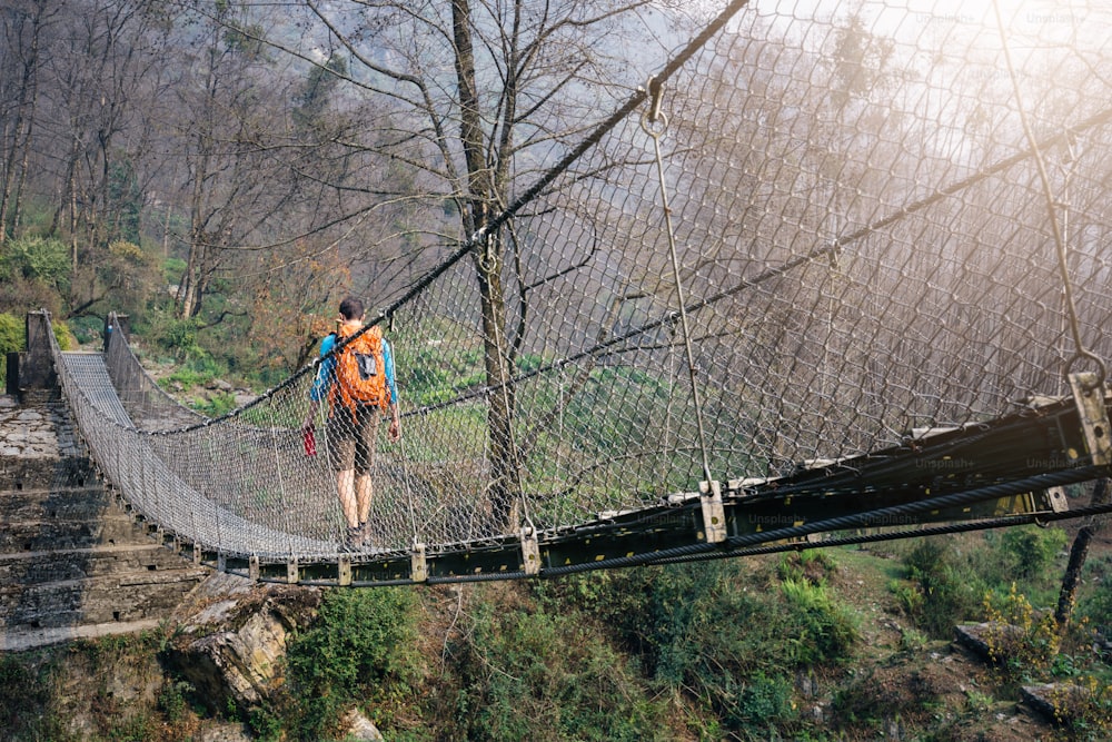 Tourist with backpack crossing suspension footbridge at Himalayas.