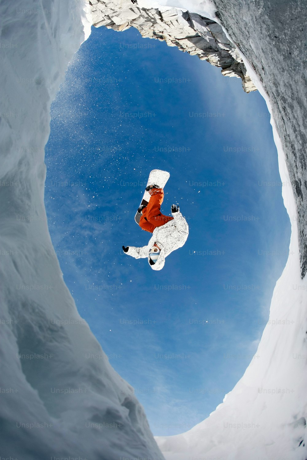 View from below of snowboarder jumping over rocky mountainside in winter