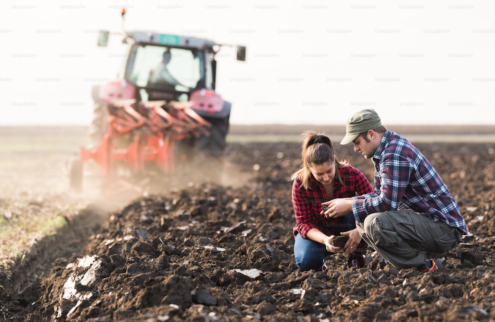 Young farmers examing dirt while tractor is plowing field