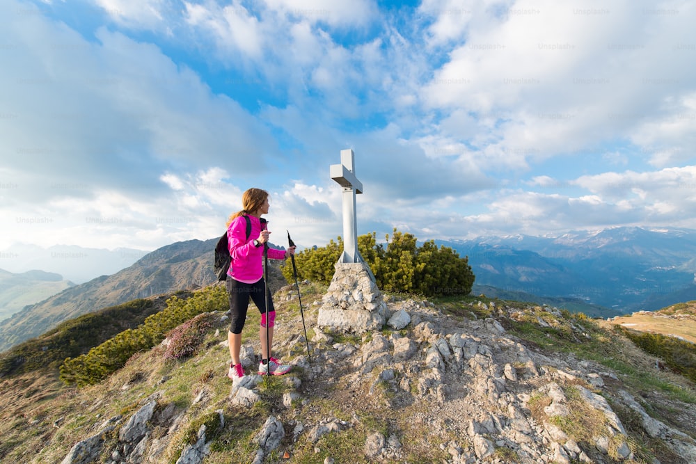 La ragazza solitaria sulla cima di una montagna con la croce osserva il paesaggio
