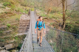 Hiker crossing suspension footbridge in Himalayas.