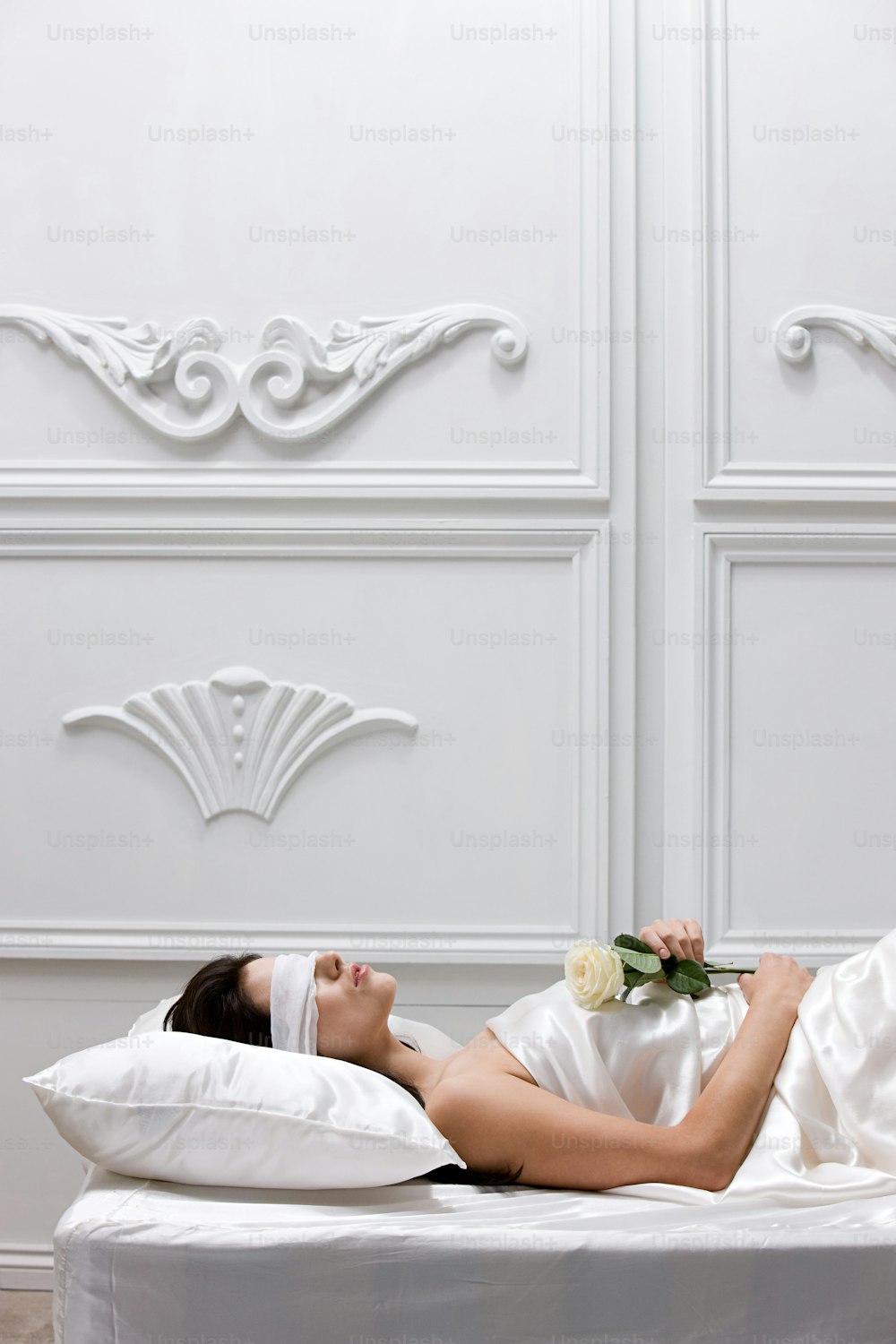 Una mujer acostada en una cama blanca con una flor en la mano