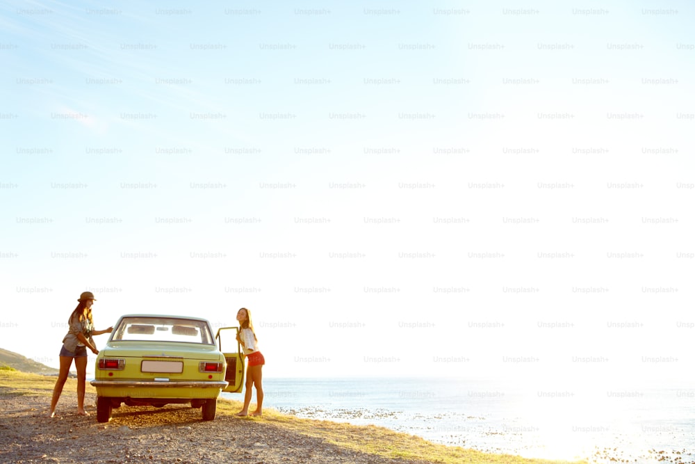 Two young woman outside of their car at the beach after a roadtrip