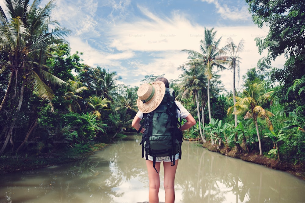 Donna viaggiatrice con zaino in piedi vicino al fiume tropicale (colore vintage intenzionale)