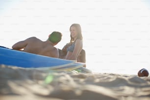 a man and a woman sitting on a beach next to a surfboard