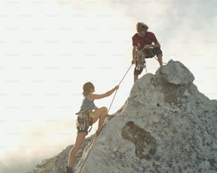 a man helping a woman climb up the side of a mountain